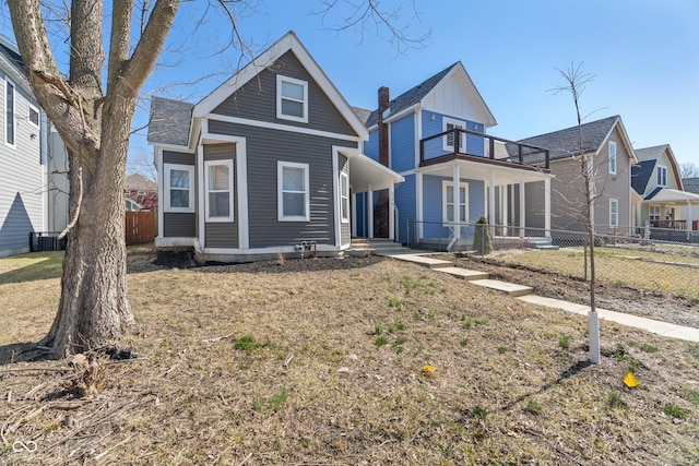 view of front facade featuring central air condition unit, a balcony, a front yard, and fence