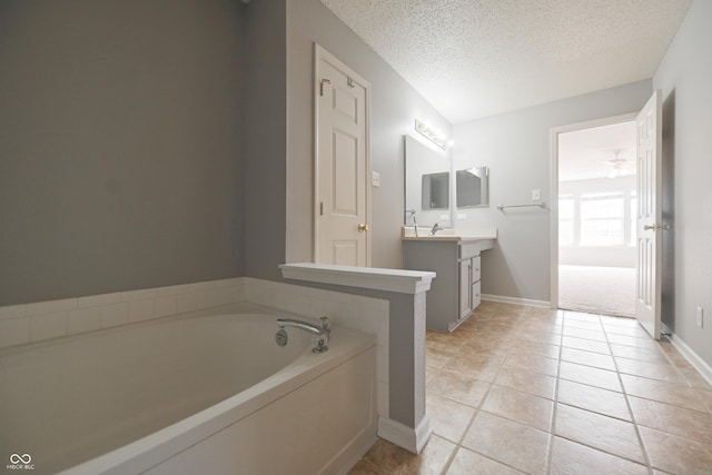 bathroom with a textured ceiling, tile patterned flooring, a garden tub, vanity, and baseboards