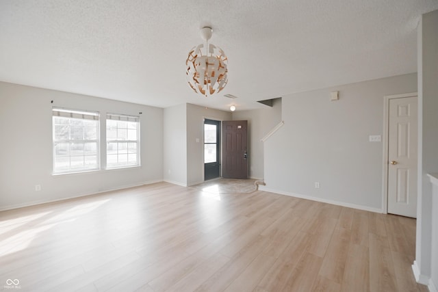 unfurnished room with light wood-style floors, a textured ceiling, and baseboards