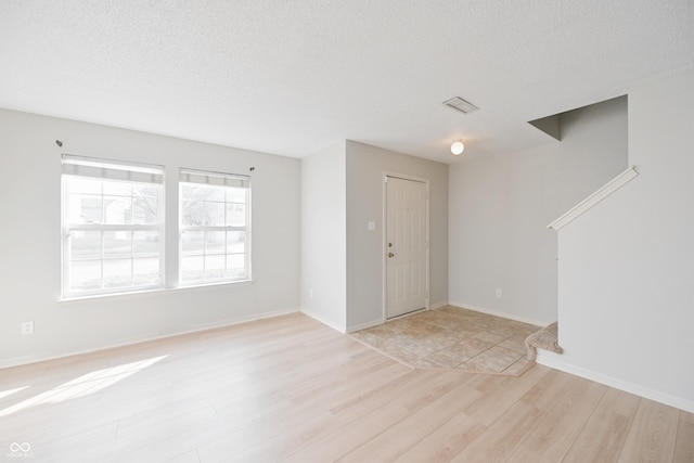 entryway featuring baseboards, visible vents, light wood-style flooring, and a textured ceiling