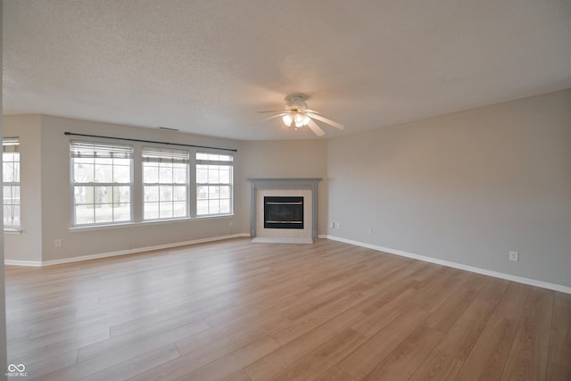 unfurnished living room with baseboards, a ceiling fan, a tile fireplace, a textured ceiling, and light wood-style floors