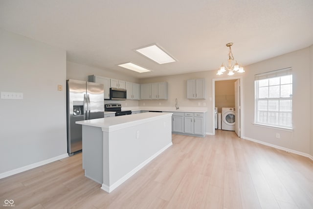 kitchen with light wood finished floors, appliances with stainless steel finishes, washing machine and clothes dryer, light countertops, and a sink