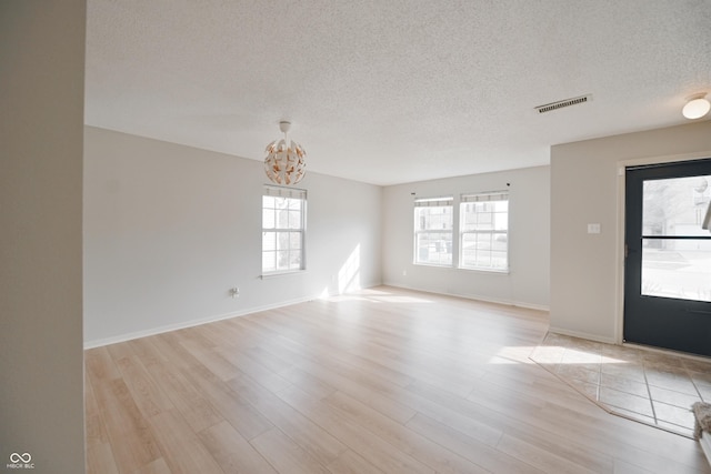 spare room featuring light wood finished floors, visible vents, an inviting chandelier, a textured ceiling, and baseboards