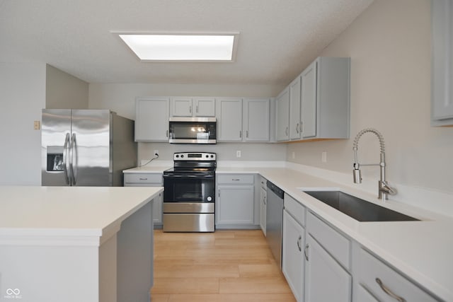 kitchen with light wood finished floors, light countertops, appliances with stainless steel finishes, and a sink