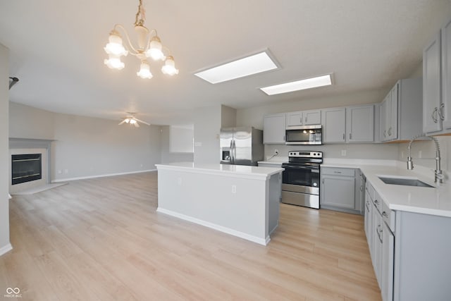 kitchen with light countertops, gray cabinets, stainless steel appliances, a sink, and a high end fireplace