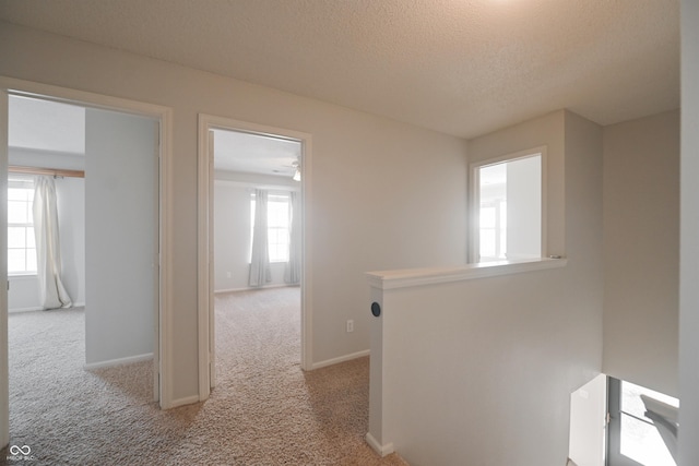 hall featuring baseboards, a textured ceiling, and light colored carpet