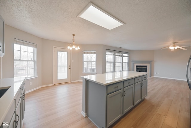 kitchen featuring a glass covered fireplace, open floor plan, light countertops, gray cabinets, and light wood-type flooring