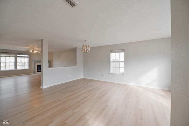 unfurnished living room featuring light wood-style floors, ceiling fan with notable chandelier, a textured ceiling, and a glass covered fireplace