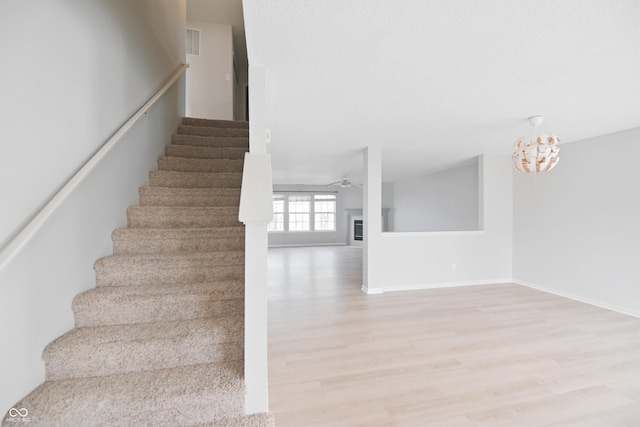 stairway featuring a fireplace, visible vents, a ceiling fan, wood finished floors, and baseboards