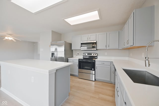 kitchen featuring stainless steel appliances, a ceiling fan, a kitchen island, a sink, and light wood-type flooring