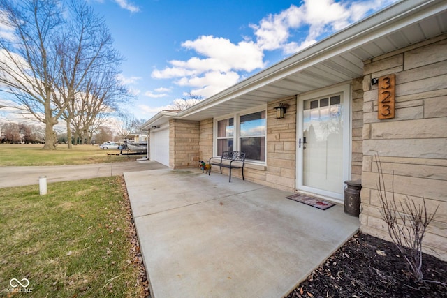 entrance to property featuring driveway, stone siding, a garage, and a yard