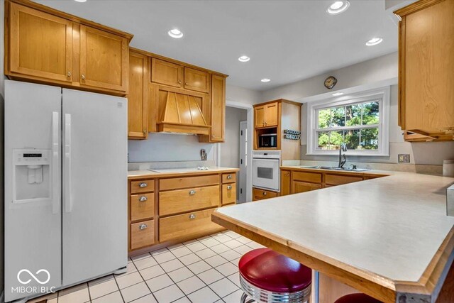 kitchen featuring light countertops, a peninsula, custom exhaust hood, white appliances, and a sink