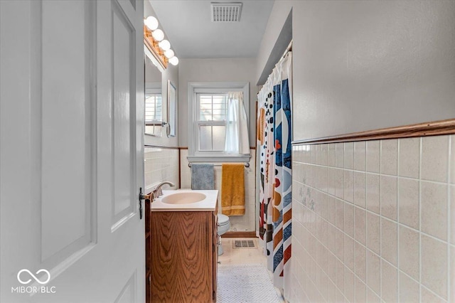 full bathroom with tile walls, toilet, visible vents, and wainscoting