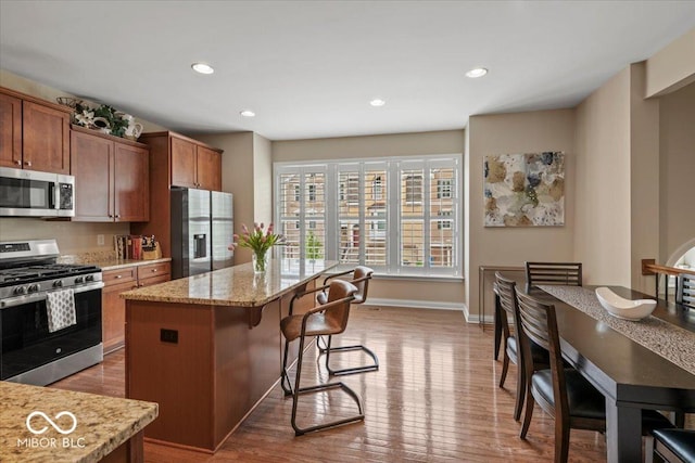 681 Greenford Trl N, Carmel, IN 46032 - kitchen featuring appliances with stainless steel finishes, a kitchen bar, a kitchen island, wood finished floors, and light stone counters