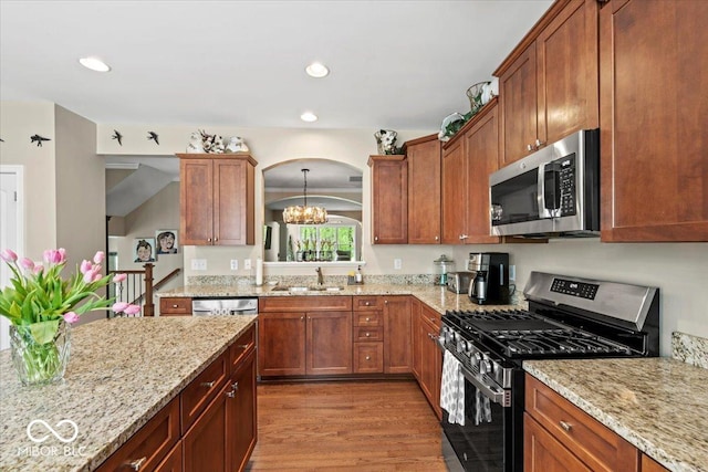 681 Greenford Trl N, Carmel, IN 46032 - kitchen with appliances with stainless steel finishes, a chandelier, arched walkways, light stone countertops, and wood finished floors