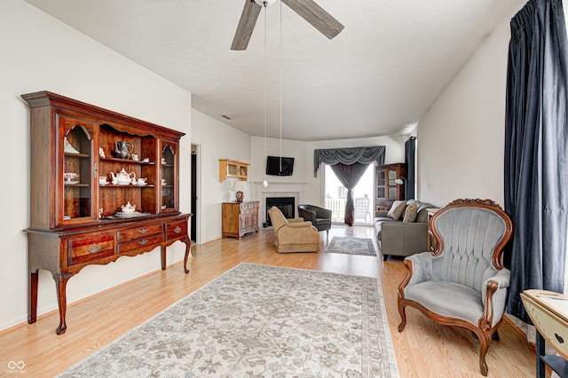 living area with a tiled fireplace, a textured ceiling, light wood finished floors, baseboards, and ceiling fan