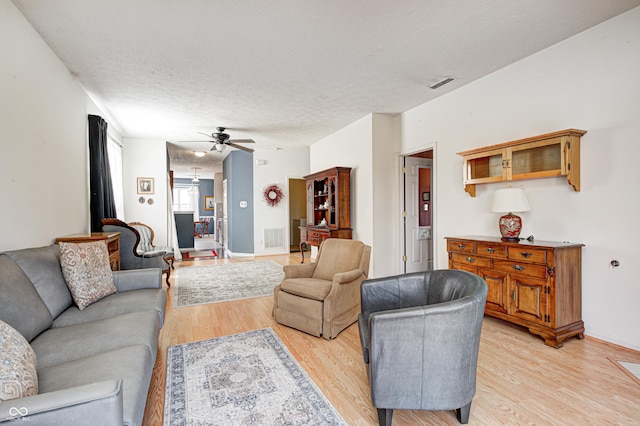 living area featuring visible vents, a textured ceiling, a ceiling fan, and light wood finished floors