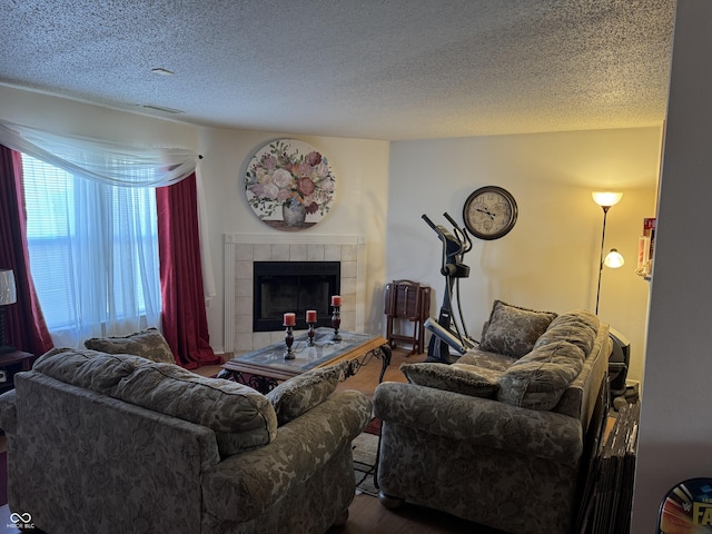 living room with a textured ceiling, wood finished floors, visible vents, and a tile fireplace