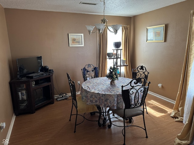 dining space with visible vents, baseboards, a textured ceiling, and wood finished floors