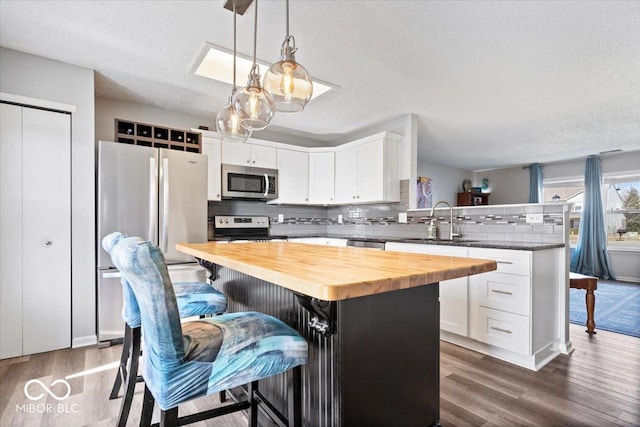 kitchen featuring dark wood-type flooring, butcher block counters, a peninsula, stainless steel appliances, and a sink