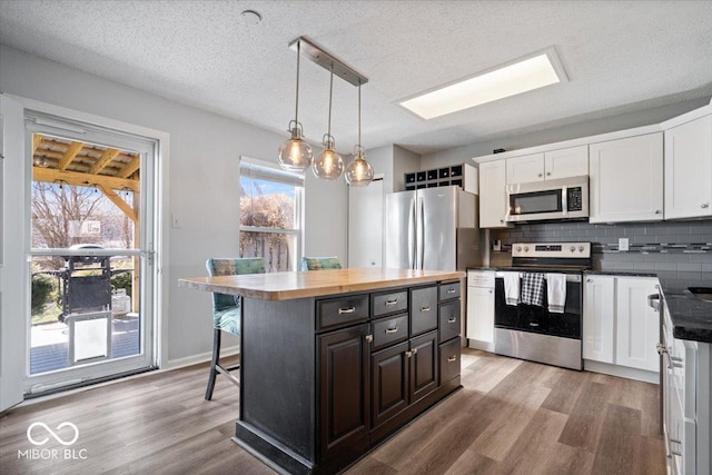 kitchen with light wood-type flooring, appliances with stainless steel finishes, a breakfast bar area, white cabinets, and decorative backsplash