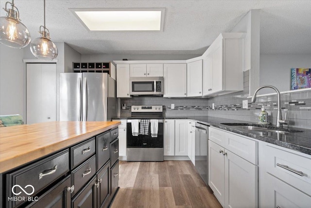 kitchen featuring white cabinets, appliances with stainless steel finishes, butcher block counters, and a sink