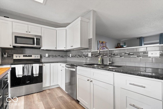 kitchen with dark stone countertops, light wood finished floors, a sink, white cabinets, and appliances with stainless steel finishes