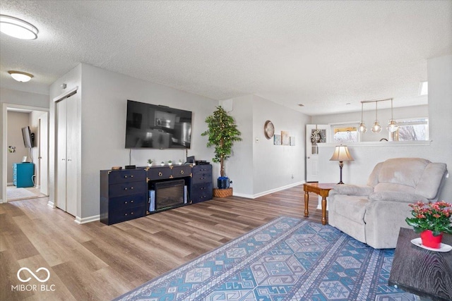 living area with a glass covered fireplace, a textured ceiling, baseboards, and wood finished floors