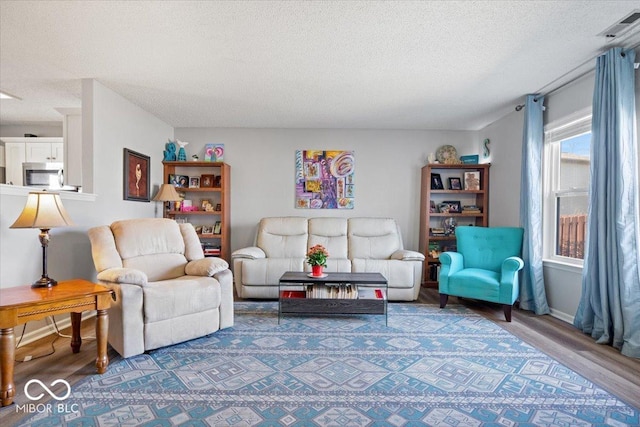 living area with visible vents, baseboards, a textured ceiling, and wood finished floors