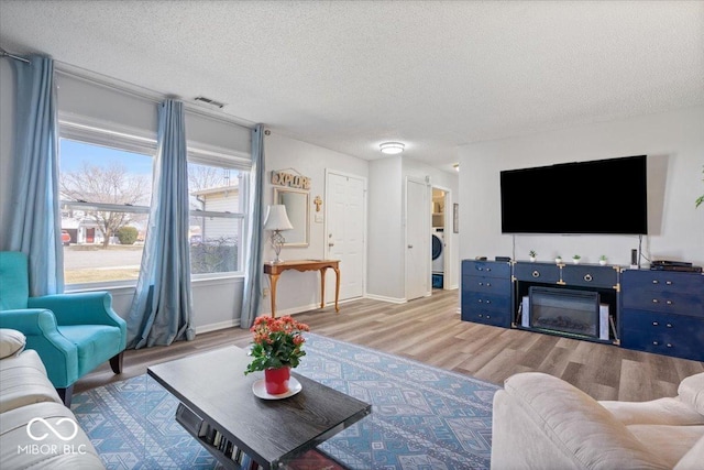 living room featuring visible vents, a textured ceiling, wood finished floors, a fireplace, and baseboards