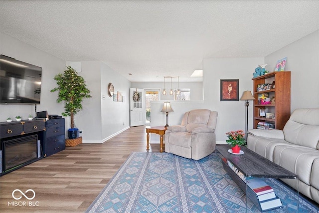 living area with baseboards, a textured ceiling, an inviting chandelier, and wood finished floors