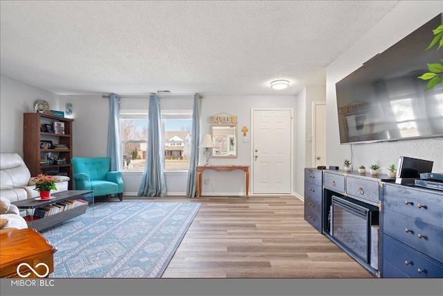 living room featuring baseboards, a textured ceiling, and light wood-style flooring