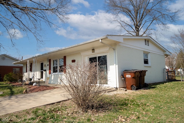 view of side of home with a yard, brick siding, and covered porch