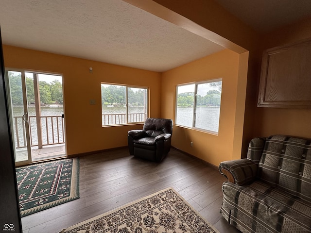 sitting room featuring a water view, a textured ceiling, baseboards, and hardwood / wood-style flooring