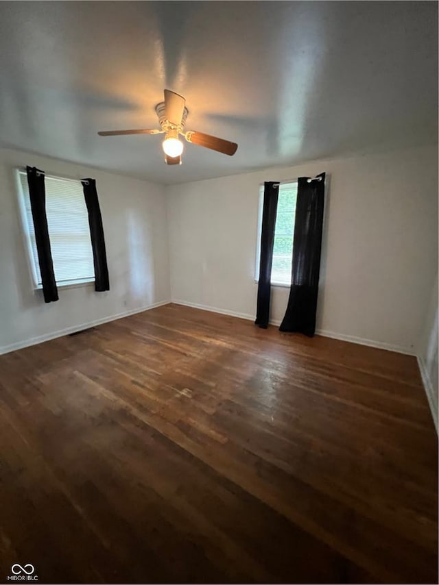 spare room featuring ceiling fan, dark wood-style flooring, and baseboards