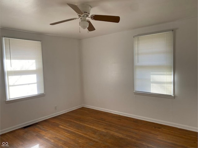 empty room with dark wood-style floors, baseboards, visible vents, and ceiling fan