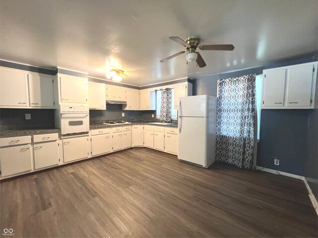 kitchen with white appliances, dark countertops, dark wood-style flooring, under cabinet range hood, and a sink