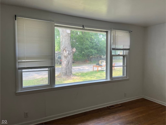 empty room featuring plenty of natural light, wood finished floors, and visible vents