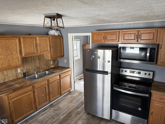 kitchen featuring a textured ceiling, a sink, appliances with stainless steel finishes, dark wood-style floors, and brown cabinetry