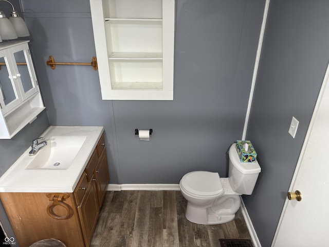 half bathroom with visible vents, toilet, vanity, wood finished floors, and baseboards