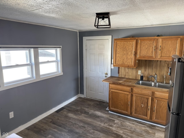 kitchen with dark wood-type flooring, brown cabinetry, a sink, and freestanding refrigerator