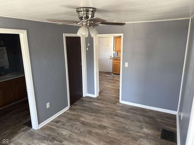 spare room featuring ceiling fan, a sink, visible vents, baseboards, and dark wood finished floors