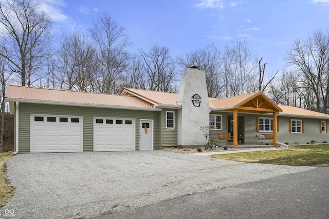 ranch-style house featuring gravel driveway, metal roof, a chimney, and an attached garage