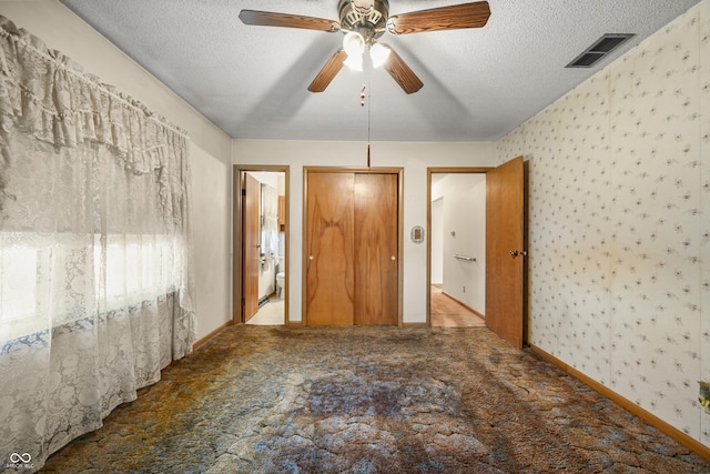 unfurnished bedroom with a textured ceiling, wallpapered walls, and carpet