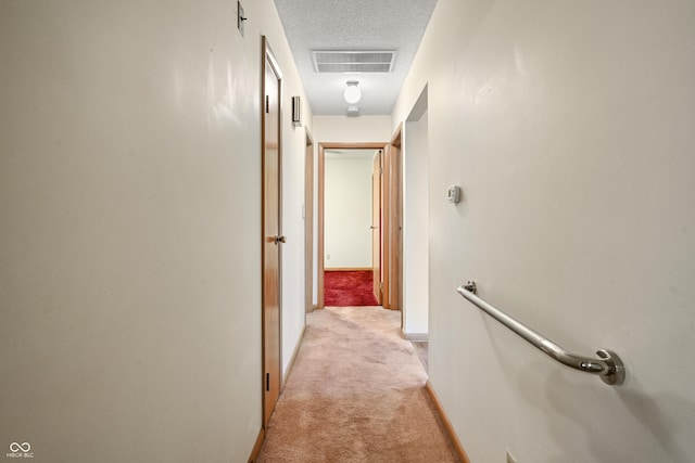 corridor featuring visible vents, light colored carpet, a textured ceiling, and baseboards