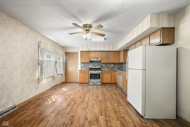 kitchen with stainless steel range with gas cooktop, wallpapered walls, light wood-style flooring, freestanding refrigerator, and under cabinet range hood