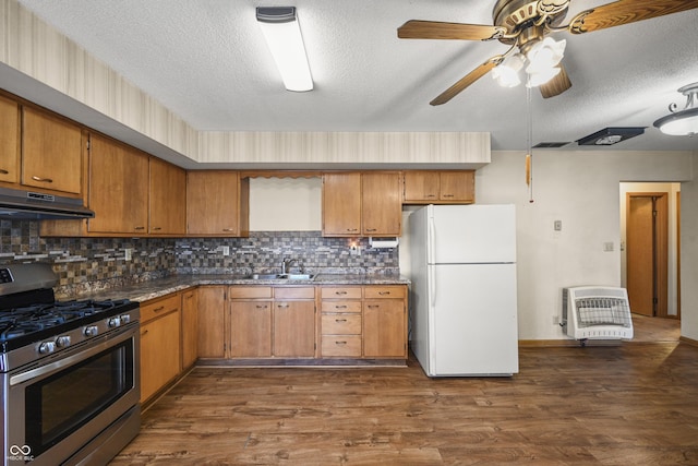 kitchen with under cabinet range hood, stainless steel range with gas stovetop, freestanding refrigerator, heating unit, and dark wood-style flooring