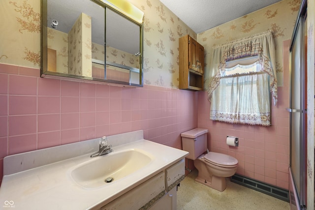 bathroom with a shower stall, wallpapered walls, toilet, wainscoting, and a textured ceiling