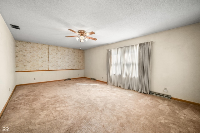 carpeted empty room with visible vents, baseboards, a textured ceiling, and ceiling fan