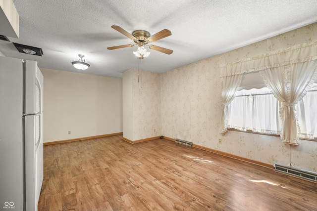 unfurnished room with a textured ceiling, visible vents, light wood-style floors, and wallpapered walls